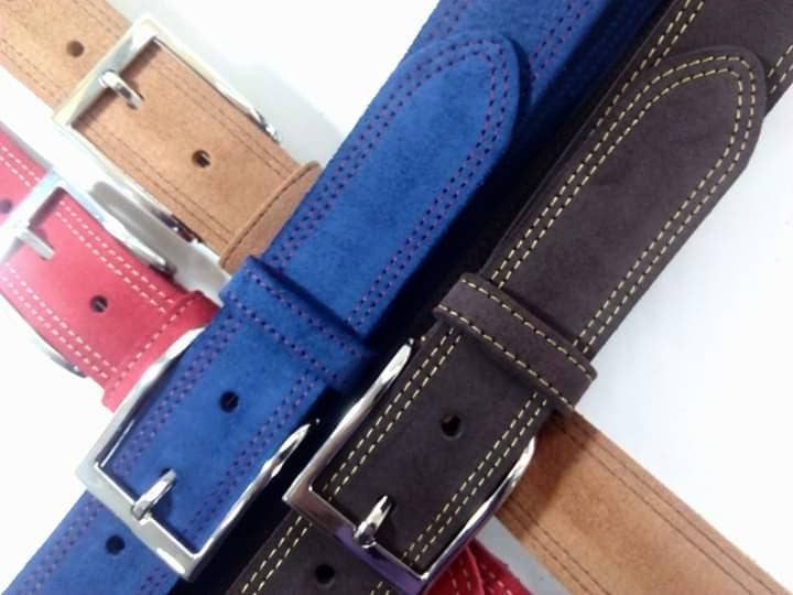 Four Creaciones Corpas Handcrafted Nubuck Leather Belt 3.5 cm in red, tan, blue, and dark brown overlap to display their metal buckles and stitched details—artisanal belts made in Spain for timeless style.