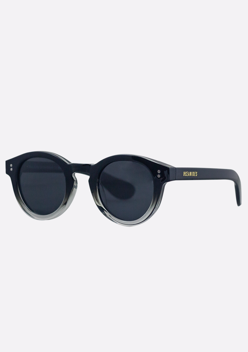 Shiny Black Rodea Sunglasses by Oceanides feature polarized lenses and glossy recycled plastic frames, with "OCEANIDES" in yellow on the left arm, shown on a plain white background.