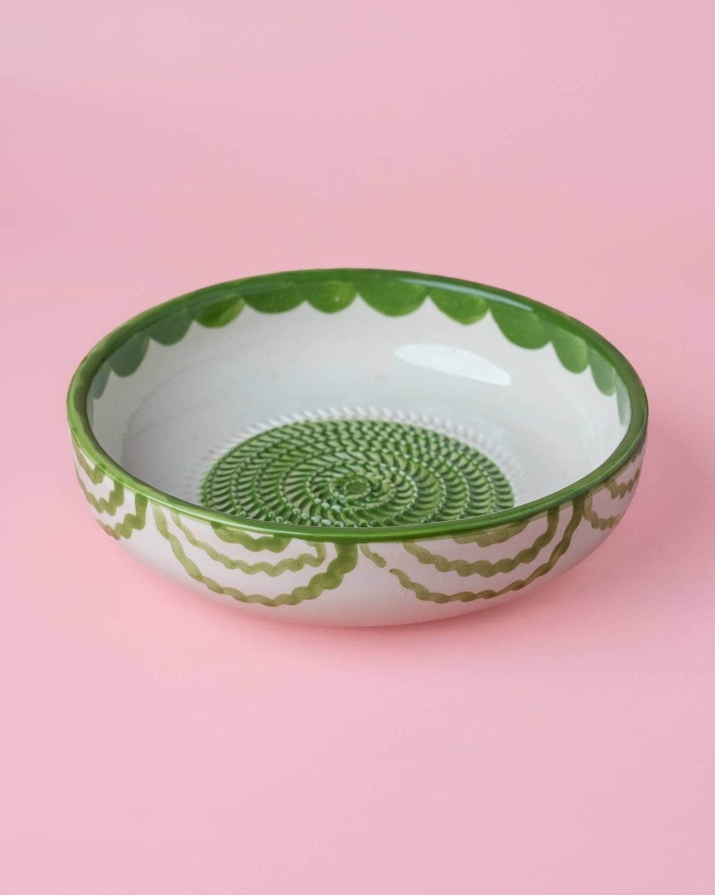 The Large Pottery Grater Plate - Roots by Iberica features green decorative patterns on a shallow, round handcrafted bowl, displayed against a pink background.
