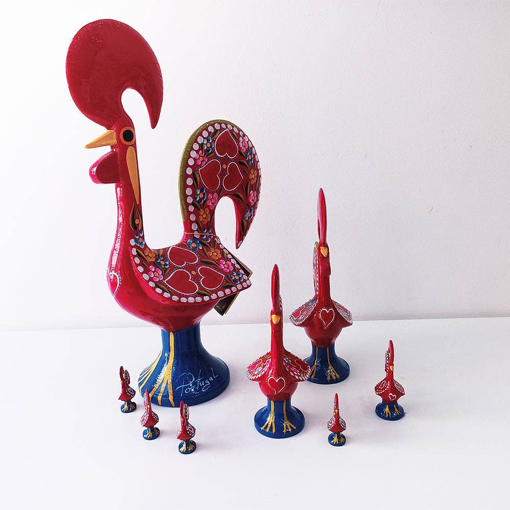 A group of colorful Iberica - Pretty things from Portugal Barcelos Rooster figurines, inspired by Portuguese art and painted in red, blue, and yellow with heart and dot patterns, are displayed on a white surface against a plain background.