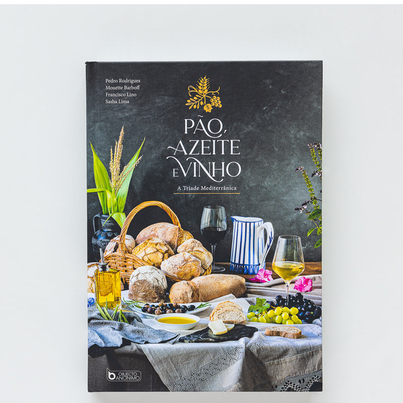 The “Bread, Olive Oil & Wine” cookbook by ObjectoAnonimo features a cover with breads, cheese, grapes, olive oil, a wine glass and pitcher on a rustic table against a dark background, evoking the Mediterranean diet.