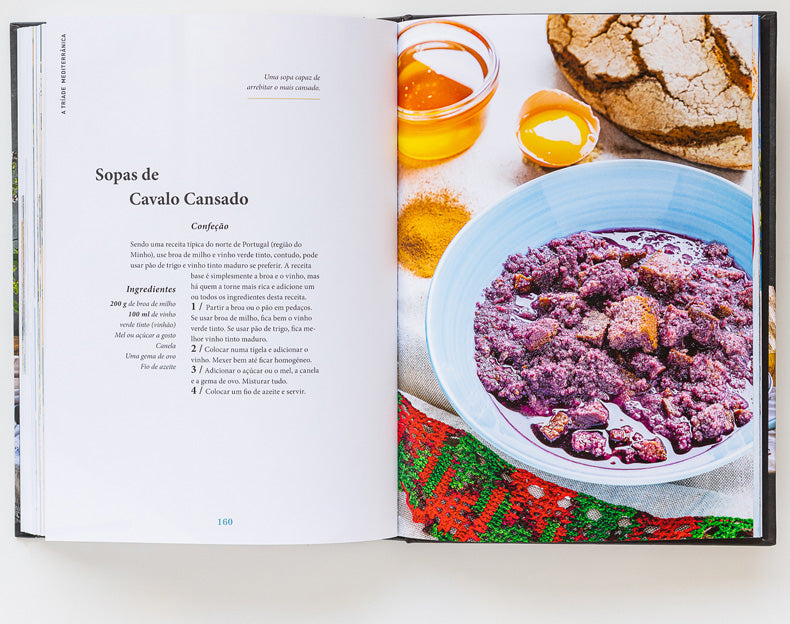 An open cookbook features Sopas de Cavalo Cansado on the left and a photo of the finished dish with Bread, Olive Oil & Wine by ObjectoAnonimo in a purple bowl on the right, all arranged atop a colorful cloth.