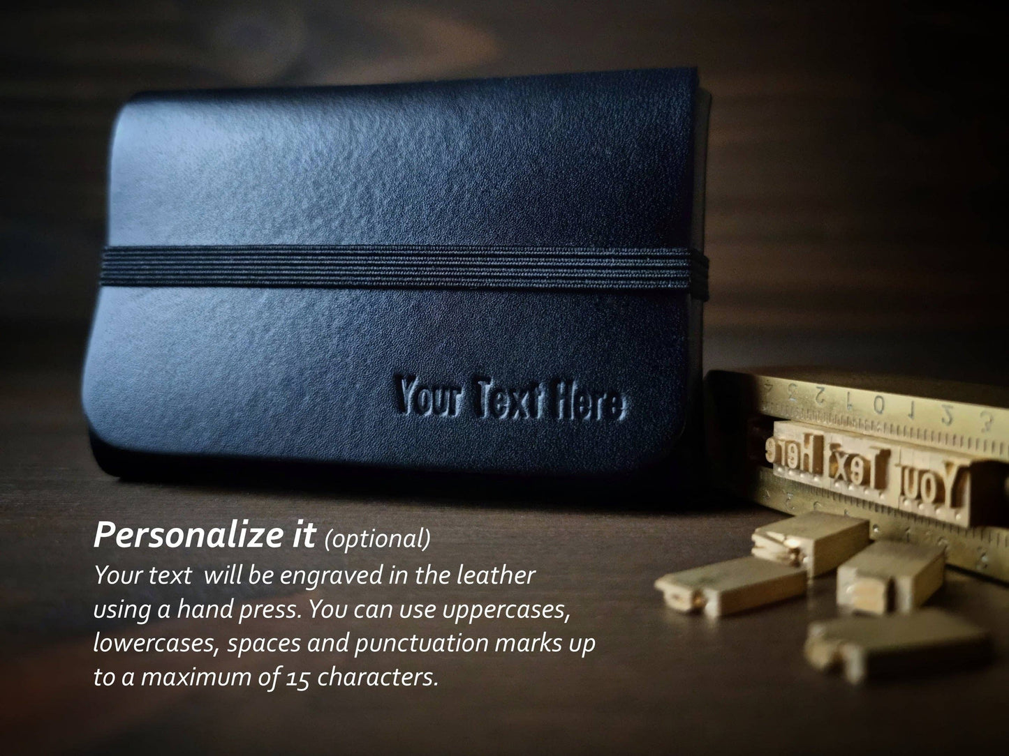 A Singular Leather Carbon Black Leather Wallet, crafted from vegetable-tanned leather and embossed with your text (up to 15 characters), rests by metal letterpress blocks on wood. RFID protection included.