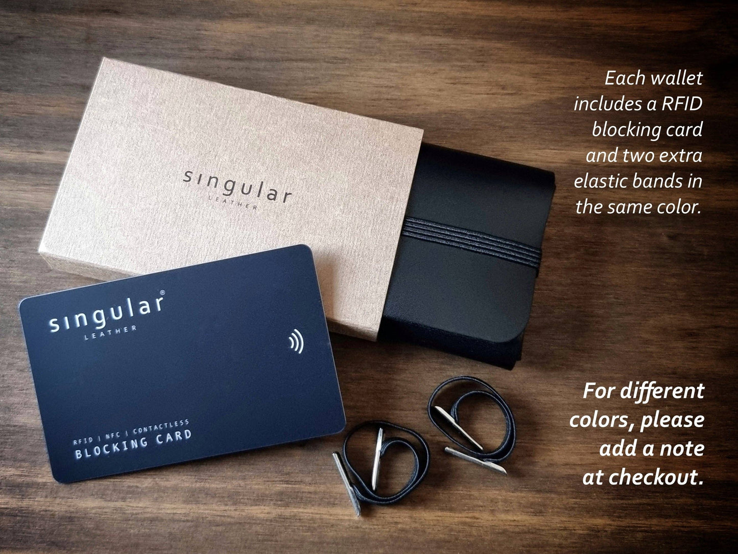 A Singular Leather Carbon Black Leather Wallet with RFID protection sits on a wooden surface, accompanied by a beige wallet box, extra elastic bands, two metallic rings, and printed product instructions and details.