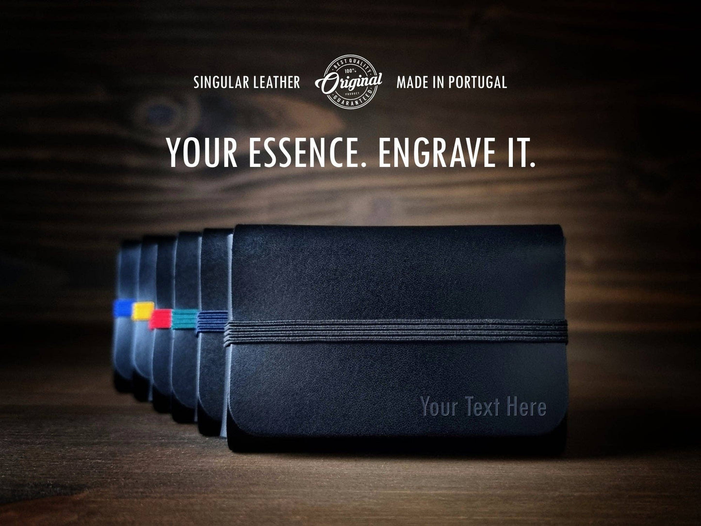 A row of Singular Leather Carbon Black Leather Wallets with colored bands is displayed on wood. The text above reads: “Your Essence. Engrave It. Singular Leather. Made in Portugal.” Now includes RFID protection for your security.