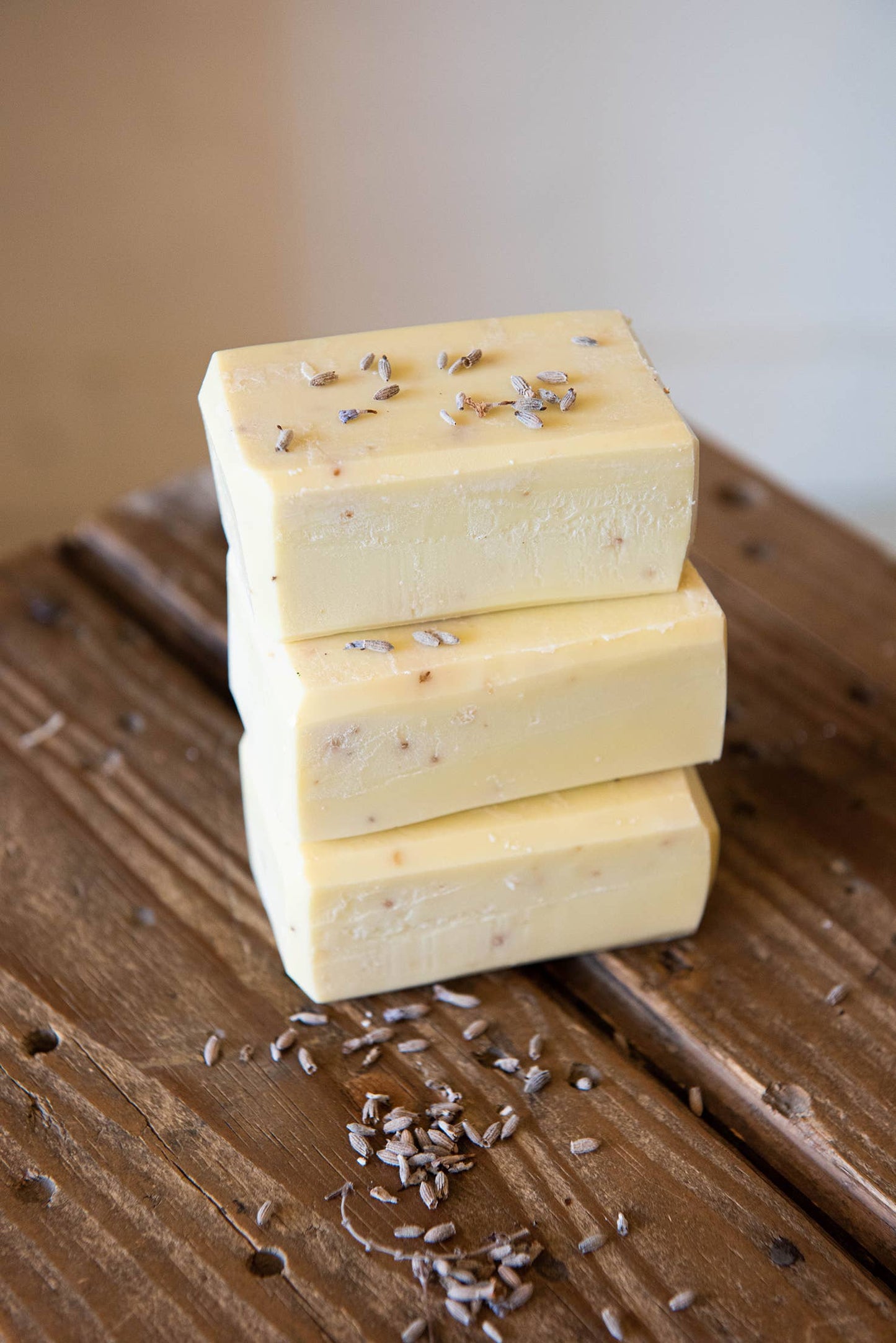Three Daki Olive Oil Soap with Lavender bars, featuring visible buds, are stacked on a rustic wooden surface with scattered lavender—ideal for gentle, hydrating care.