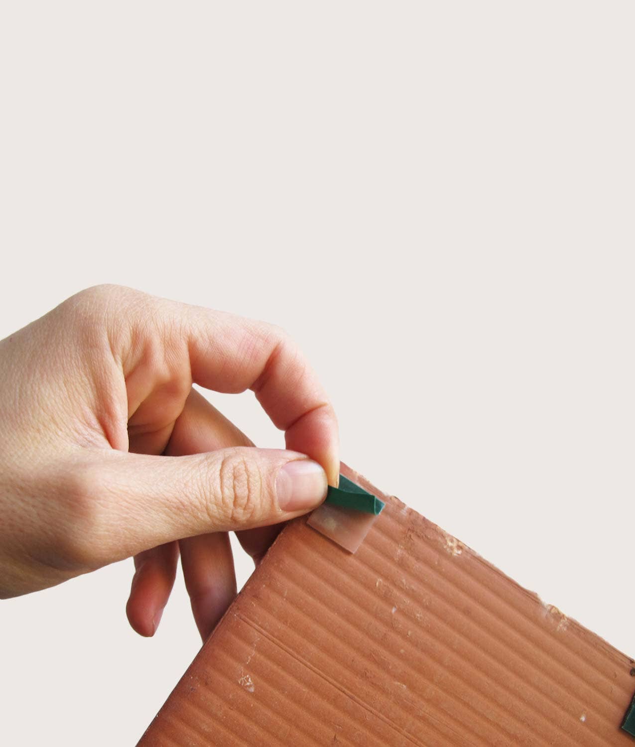 A hand peels a small piece of tape from a brown cardboard sheet, resembling the setup for the Bussoga Self Adhesive Wall Mural 3 Tiles, Bullet Man, against a plain light background.