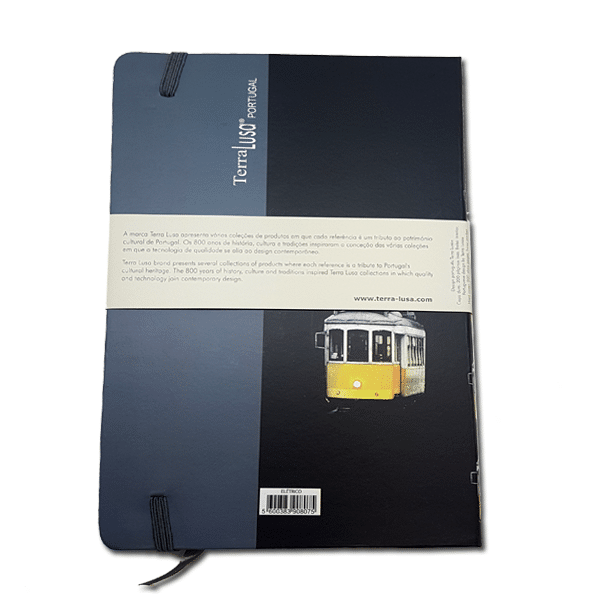 A dark blue and black Tram Notebook by Terra Lusa features a yellow tram on the cover, an elastic band, and a white paper band with text and branding, celebrating Portuguese cultural heritage.