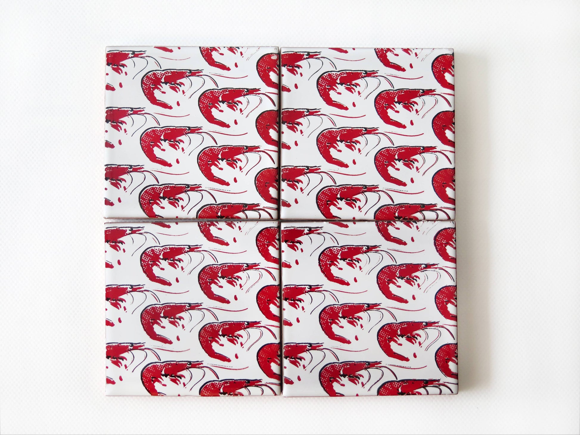 Four Gamba Design Ceramic Coasters by Bussoga, handmade in Spain, are wrapped in white paper featuring a red shrimp pattern and arranged in a tidy 2x2 grid on a white background.