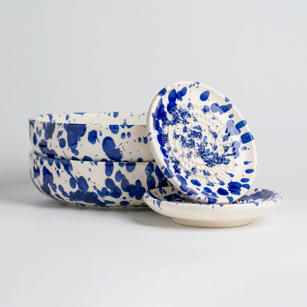 The Handmade cheese and vegetable grater plate - PERSIA by Tierra Cocida features bold blue splatters on white ceramic—a handmade Spanish piece that adds a striking Mediterranean touch, shown on a light background.