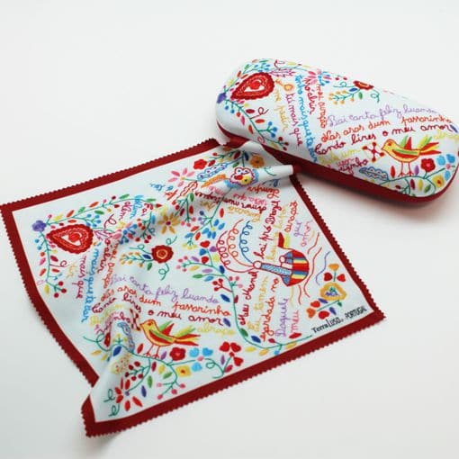 The "Lovers" Handkerchiefs Glasses Case by Terra Lusa features a vibrant glasses case and matching cloth with playful red, blue, and yellow Portuguese embroidery-inspired birds, hearts, and handwritten-style text on white with a red border.