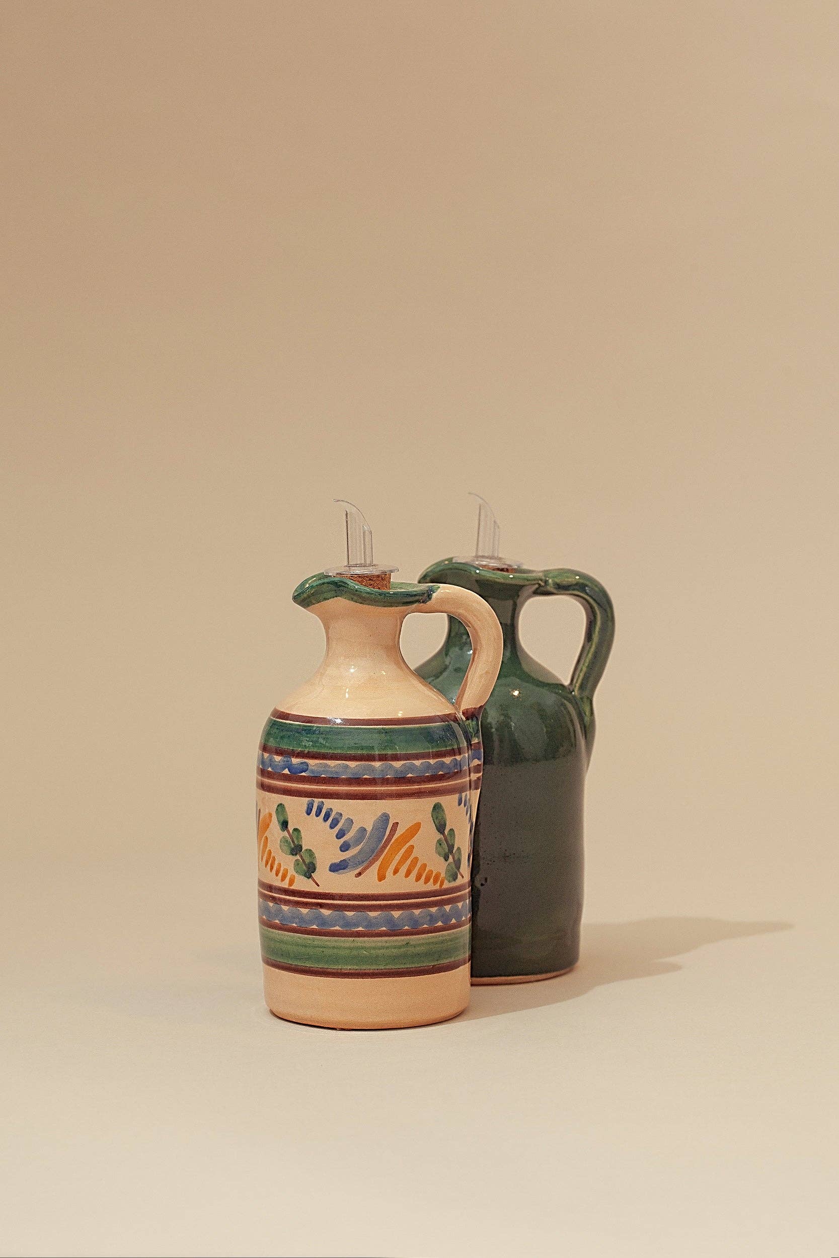 Two Eturel Madrid Medina Oil Mill ceramic dispensers, inspired by Andalusian tradition, stand on a plain background—one displays colorful patterns from the Medina collection, while the other is finished in solid dark green.