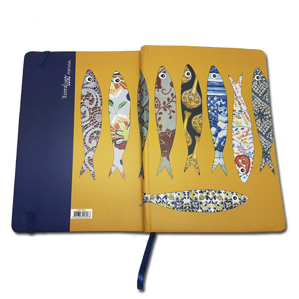 The Terra Lusa Sardines Notebook features a yellow cover with vibrant fish patterns inspired by Lisbon and Portuguese culture. It is partially open, showing a blue back cover and a blue ribbon bookmark.