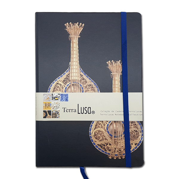The Fado Notebook by Terra Lusa features two ornate Portuguese guitars on its black cover, celebrating Portuguese cultural heritage. Secured with a blue elastic band and wrapped in a branded paper sleeve.