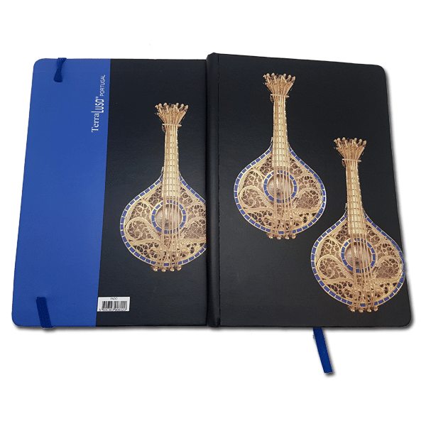 A Terra Lusa Fado Notebook with a blue spine and bookmark is open, showing a cover decorated with three gold mandolins—a refined nod to Portuguese heritage.