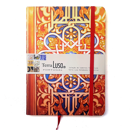 The Terra Lusa Stained Glass Notebook features a vibrant, tile-inspired cover with a red elastic band and ribbon, celebrating Portuguese Cultural Heritage. A branded label wraps the front, showcasing the product and design details.
