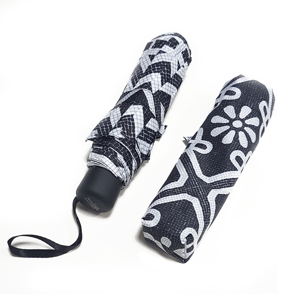 Two folded Terra Lusa Sidewalk Umbrellas, one with its cover and one without, show off striking black and white geometric and floral calçada patterns against a clean white background.