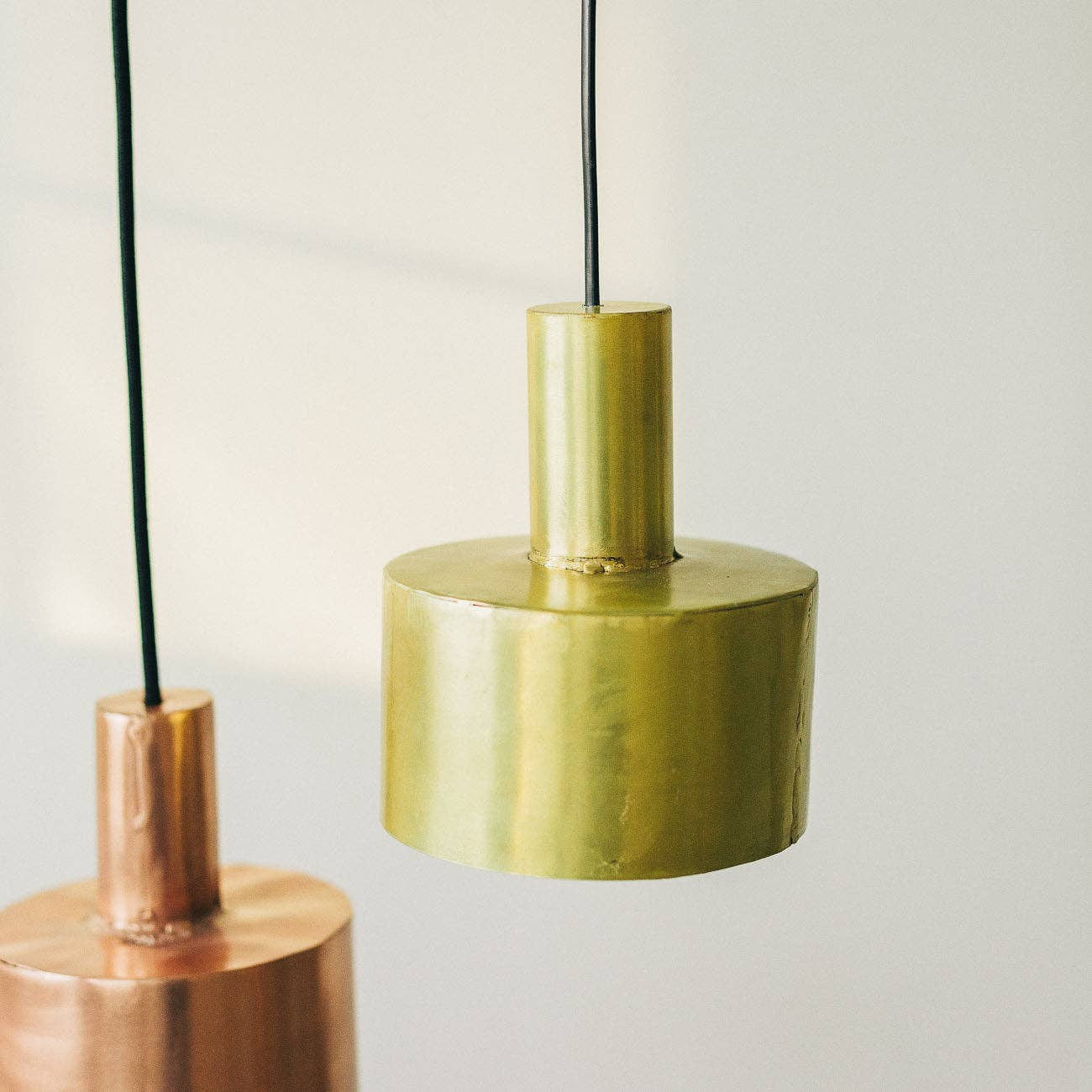 Two modern pendant lights hang from the ceiling: a Seber Lamp by Hannun with a shiny gold cylindrical shade in the foreground, and a copper-finished pendant in the background—ideal for industrial-inspired interiors.