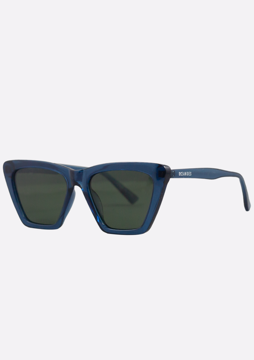 Oceanides Sunglasses (Polarized) - Perse Crystal Dark Blue Green feature blue cat-eye frames, dark tinted lenses, and a small OCEANIDS logo on the left arm. Eco-friendly design, shown on a plain white background.