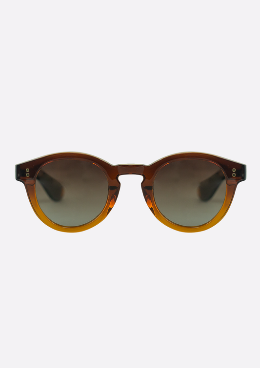 Oceanides Sunglasses (Polarized) – Rodea Crystal Gradient Brown feature a transparent amber recycled plastic frame, dark gradient lenses, and subtle metallic corner accents, shown on a plain white background.