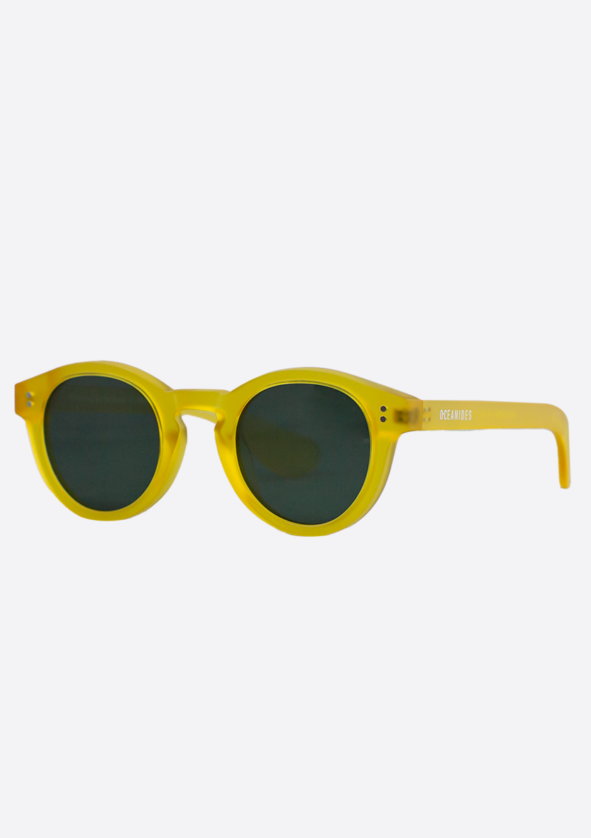The Oceanides Sunglasses (Polarized) - Rodea Yellow Frosted feature a bright yellow eco-friendly, thick frame with round dark lenses. "OCEANIDES" is printed in white on the right temple, shown against a plain white background.