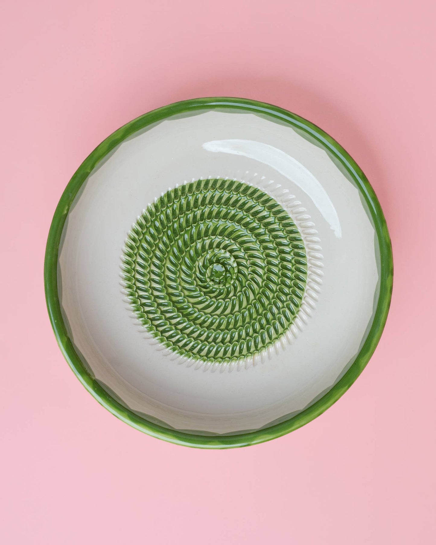 The Large Pottery Grater Plate - Roots by Iberica - Pretty things from Portugal is a handcrafted ceramic plate with a green rim and spiral center, showcased on a pink background.