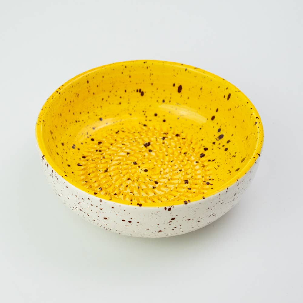The Alfar Tierra Cocida Ceramic Cheese and Vegetable Grater Plate Nuevo Canela is handmade in Spain, featuring a bright yellow interior, white exterior with brown speckles, and a textured base, set against a plain white background.