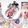 The Terra Lusa Lovers’ Handkerchiefs Eco Shopper—a reusable shopping bag and pouch with colorful floral and heart patterns—rests on a white surface. The white fabric pouch features a black clip for easy attachment.