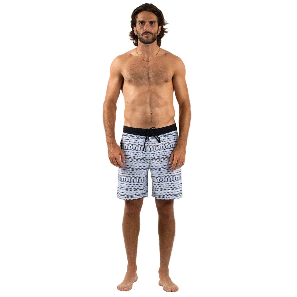 A barefoot man with long dark hair and a beard stands facing forward against a plain white background, wearing Futah’s Cacela Blue Boardshorts, which feature a patterned design and black waistband—perfect swimwear inspired by the Portuguese coast. He is shirtless.