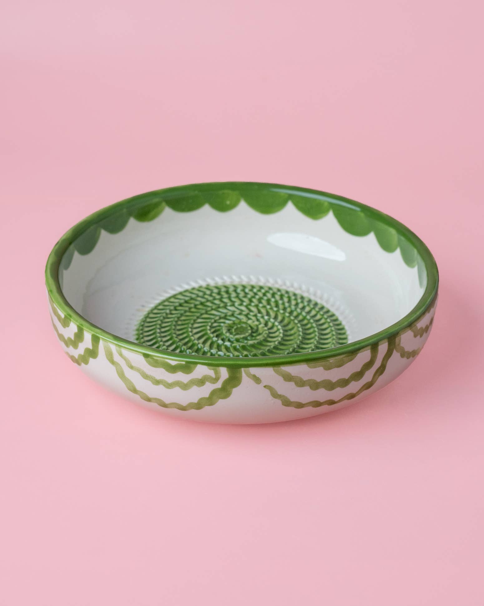 The Large Pottery Grater Plate - Roots by Iberica features green decorative patterns on a shallow, round handcrafted bowl, displayed against a pink background.