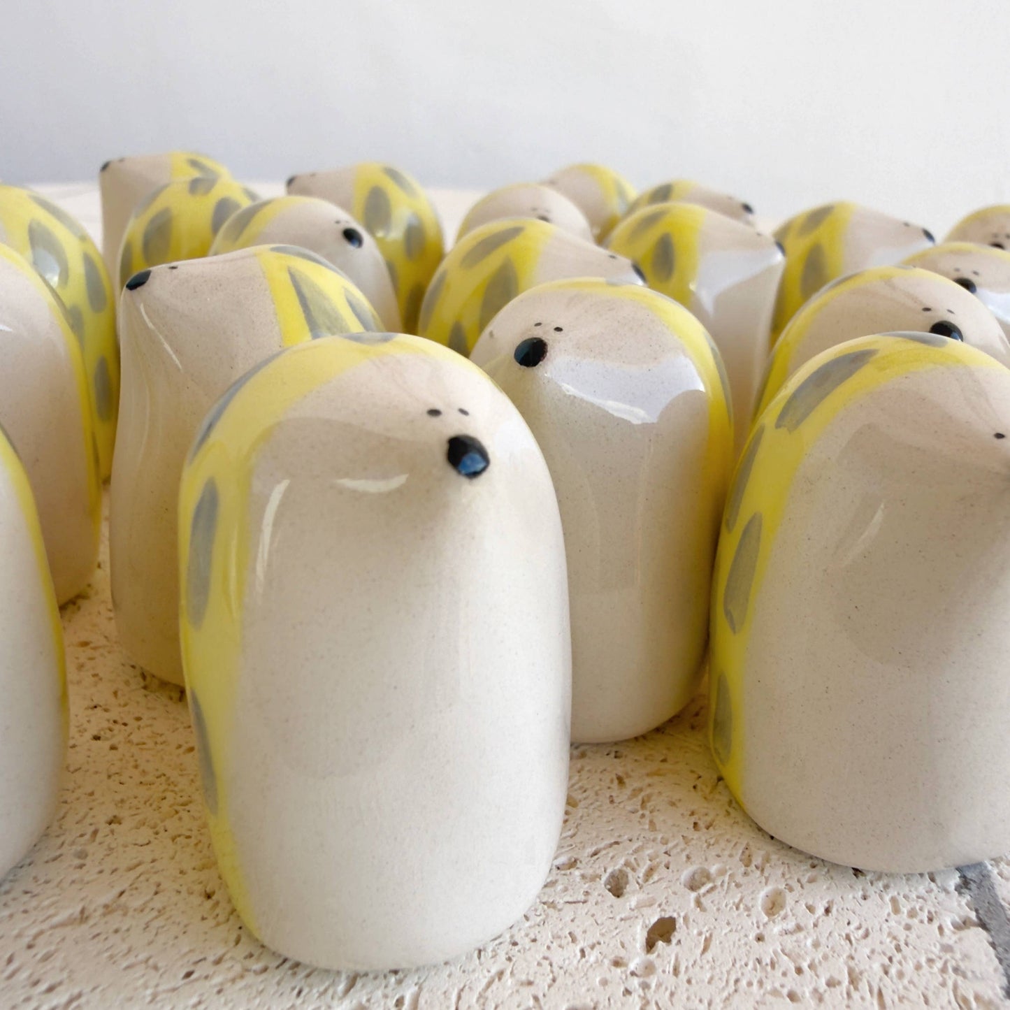 A cluster of Picuru ceramicas' Porcupine Amulet of Self-Protection—handmade ceramic figurines with cream bodies, yellow spots, and black noses—embody awareness and strength on a textured white surface.