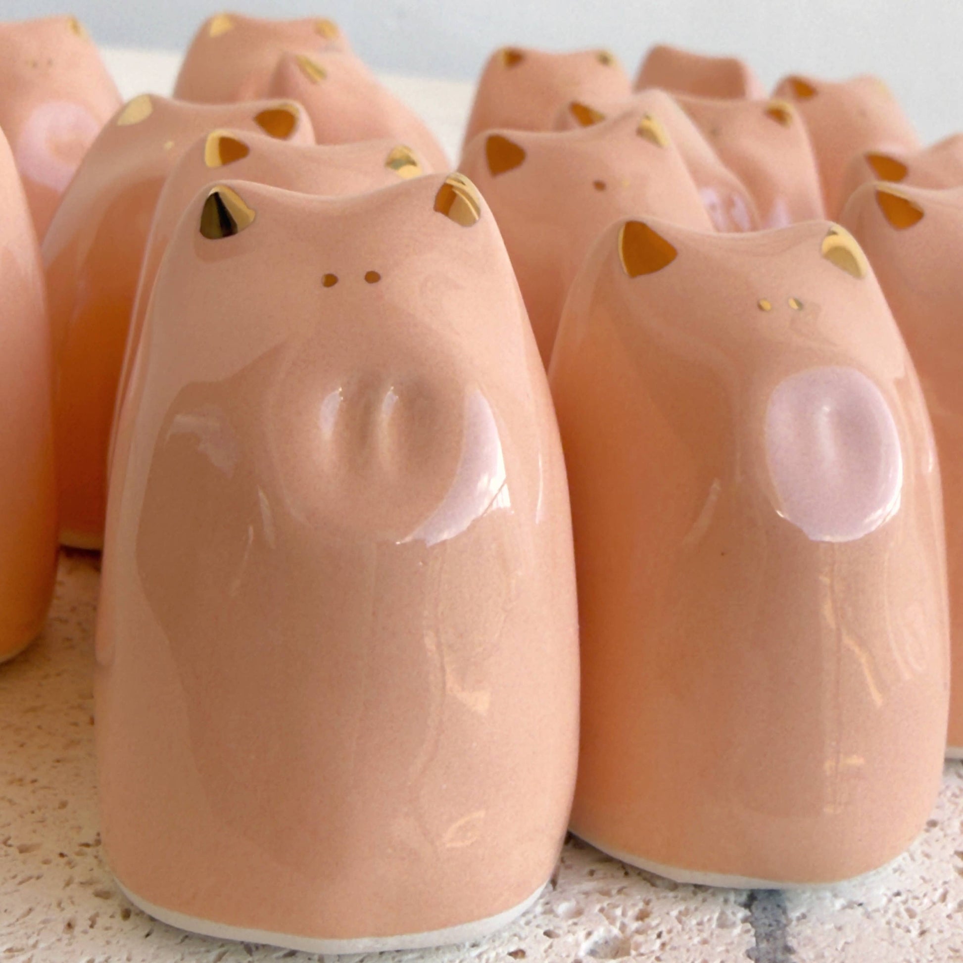 A set of glossy, gold-luster Fortune Pig Amulets by Picuru ceramicas, handcrafted with minimal features and available in 5 languages, are arranged together on a light surface.