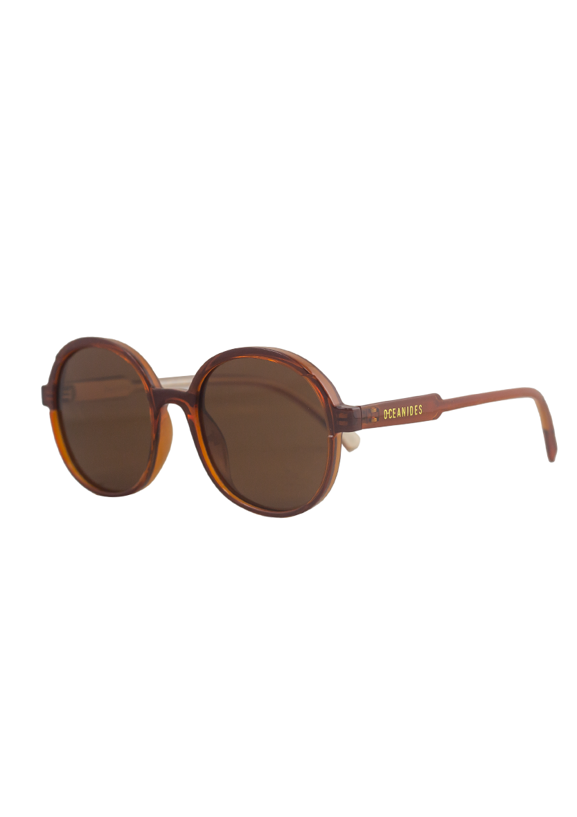 Brisa Crystal Brown Beige Sunglasses by Oceanides feature oversized round frames with dark lenses, a tortoiseshell look, and gold Oceanides branding on the temples—ideal for bold 80s-inspired style against a plain white backdrop.