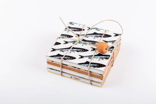 Sardines Coasters by Bussoga: a stack of handmade ceramic coasters featuring a black sardines pattern, tied with twine and a wooden bead, displayed on a white background.