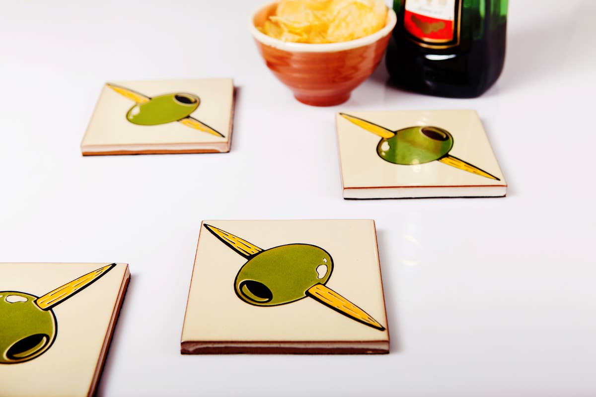 Set of four Bussoga Olivas Coasters featuring a playful green olive and toothpick design on white ceramic—perfect for adding charm to your snack and drink gatherings.