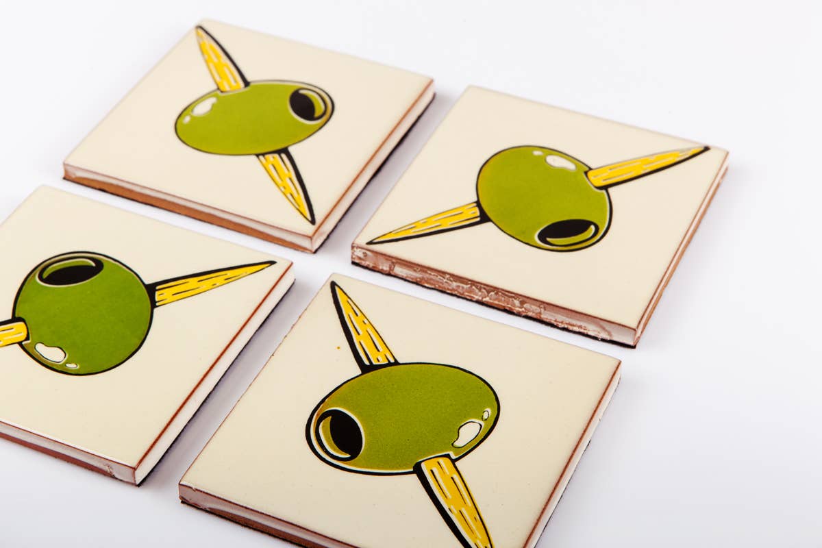 Set of four Bussoga Olivas Coasters—ceramic coasters featuring green olives on yellow toothpicks, screen-printed and elegantly arranged on a white surface.