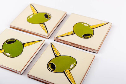 Set of four Bussoga Olivas Coasters—ceramic coasters featuring green olives on yellow toothpicks, screen-printed and elegantly arranged on a white surface.