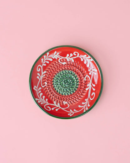 The Handmade Ceramic Grater Plate Small - Alcazaba by Alfar Tierra Cocida features a round design with a red rim, green center pattern, and white floral details—an ideal unique kitchen gift—displayed on a light pink background.