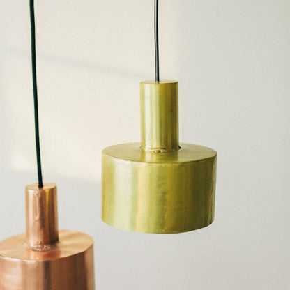Two modern pendant lights hang from the ceiling: a Seber Lamp by Hannun with a shiny gold cylindrical shade in the foreground, and a copper-finished pendant in the background—ideal for industrial-inspired interiors.