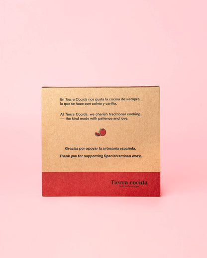 A brown and red cardboard box with Spanish and English text celebrates traditional Spanish artisan work—ideal packaging for the Alfar Tierra Cocida Handmade Ceramic Grater Plate Small - Alcazaba—shown against a pink background.