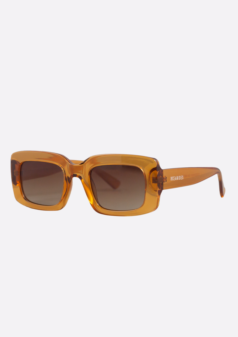 Oceanides Sunglasses (Polarized) - Ida Crystal Orange Brown feature a translucent amber rectangular frame and brown gradient polarized UV400 lenses, displayed at a slight angle on a light grey background.