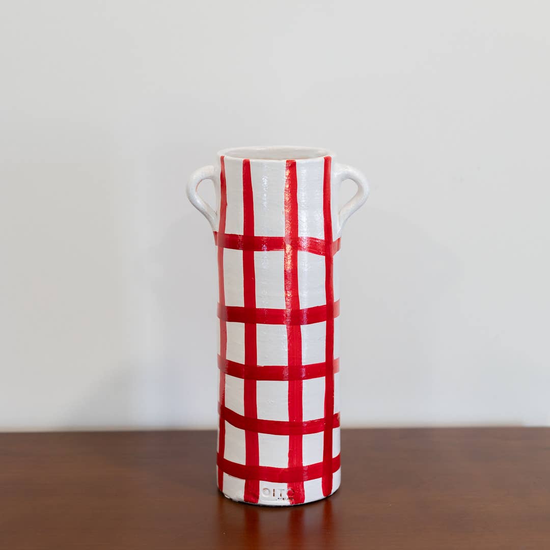 The Udine vase by OITO Atelier is a tall, white handmade ceramic piece with two small handles and a bold red grid pattern, highlighting Portuguese craftsmanship. It is shown on a wooden surface against a plain white background.