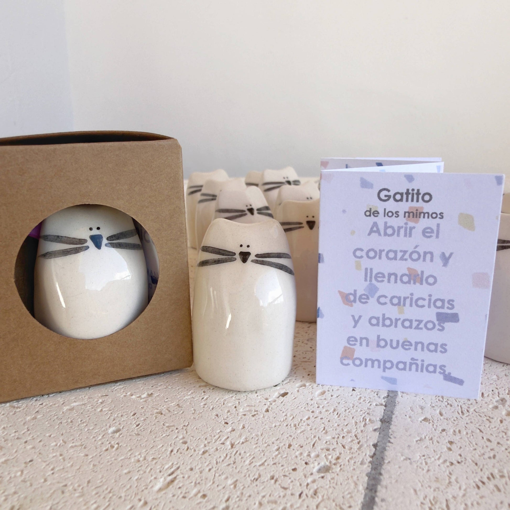 The Kitten Amulet of Cuddles by Picuru ceramicas is a handmade ceramic cat figurine in a brown box with window, accompanied by a Spanish card—an ideal friendship or comfort gift to inspire hugs and good company.