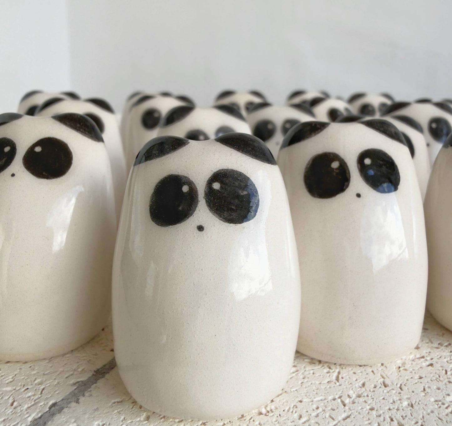 A collection of Picuru ceramicas’ Panda Amulet of Inner Peace – Handmade Lucky Charm Gifts, featuring smooth white ceramic figures with black eyes and spots, is arranged closely on a textured white surface.