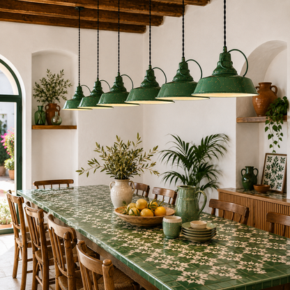 Handcrafted green enamel pendant lights suspended above a long green azulejo dining table in a Mediterranean-inspired interior with warm timber, terracotta pottery and natural textures.