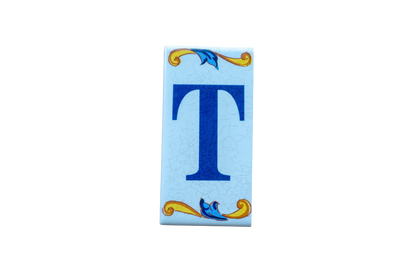 Lisa Croquets Letters – Ceramic House Letter Tiles: rectangular light blue tile featuring a dark blue T with decorative gold and blue scrollwork at the top and bottom.