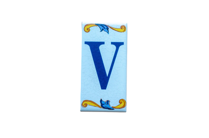Lisa Croquets Letters – Ceramic House Letter Tiles rectangular ceramic tile featuring a blue letter V with handcrafted decorative yellow and blue scrolls at the top and bottom.
