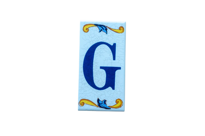 Lisa Croquets Letters – Ceramic House Letter Tile featuring a blue G, decorative blue and yellow scrollwork, and a light blue cracked background.