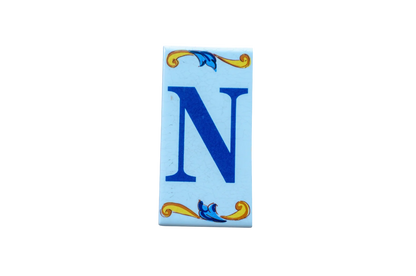 A rectangular Lisa Croquets Letters – Ceramic House Letter Tile featuring a blue capital letter N, decorated with blue and yellow scrollwork at the top and bottom.