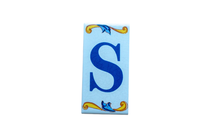 Lisa Croquets Letters – Ceramic House Letter Tiles rectangular tile featuring a blue letter S flanked by decorative yellow and blue scrollwork.
